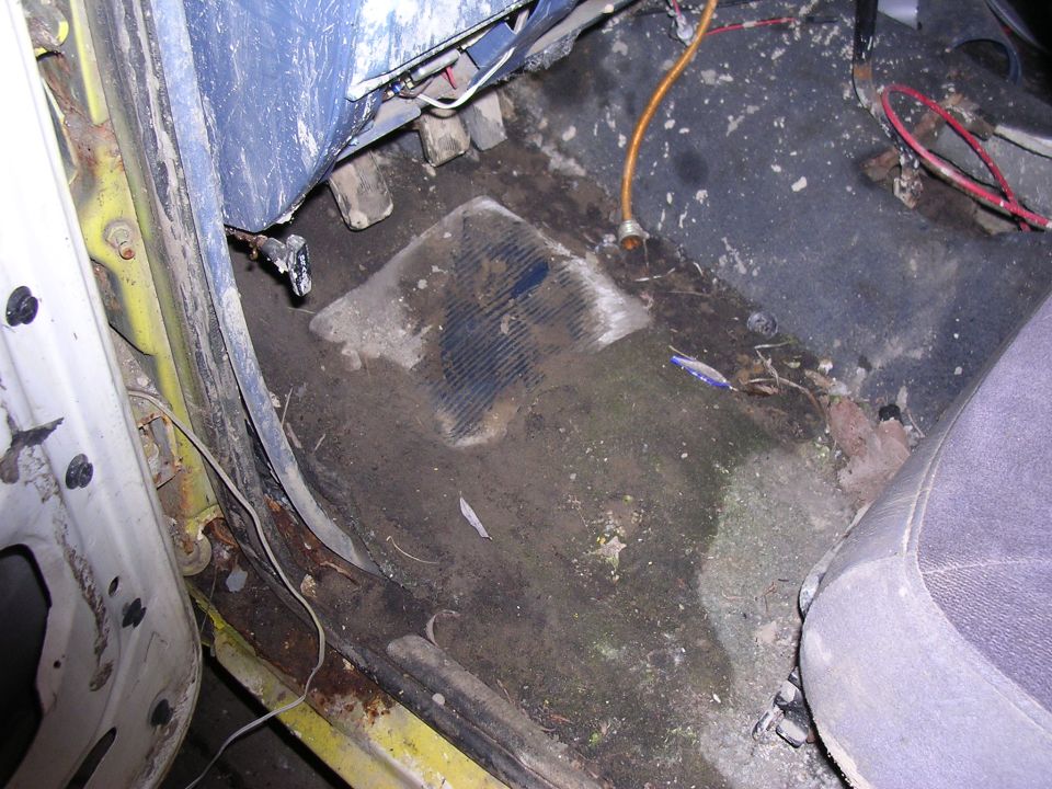 Stripped passenger floor pan with dirt, mildew and surface rust along the door sill of a white vehicle