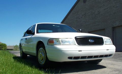 2001 Ford Crown Victoria - A white 2001 Ford Crown Victoria is parked in front of a brick building on a sunny day.