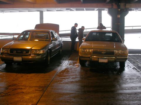 2001 Ford Crown Victoria - A 2001 Ford Crown Victoria is seen from the front with its hood open, parked alongside another vehicle.