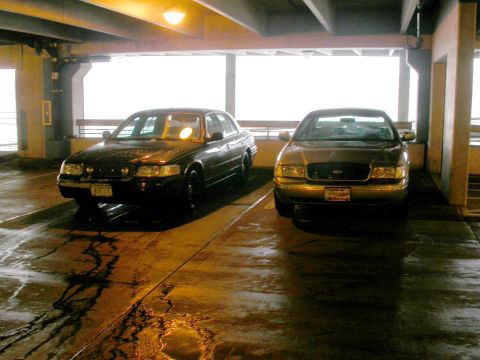 2001 Ford Crown Victoria - Two Ford Crown Victoria police cars are parked side-by-side in a dimly lit parking garage.