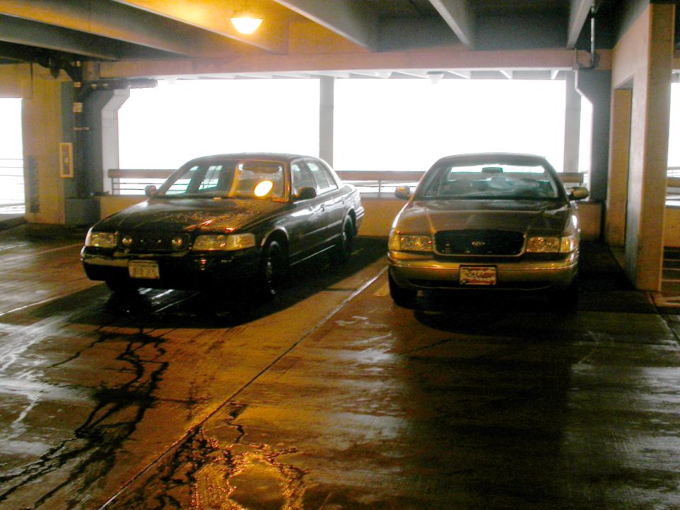 Dark and gold Ford Crown Victoria sedans parked on wet parking garage deck