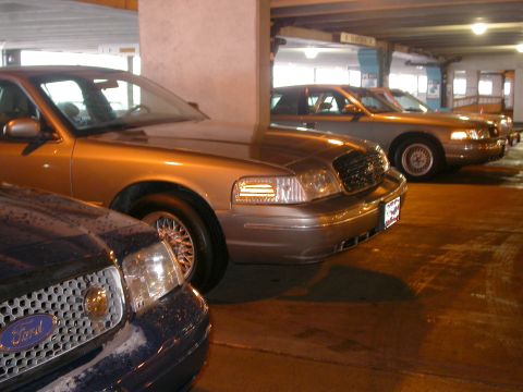 2001 Ford Crown Victoria - Multiple Ford Crown Victorias are parked in a garage, with one in the foreground showing its grille and headlights.