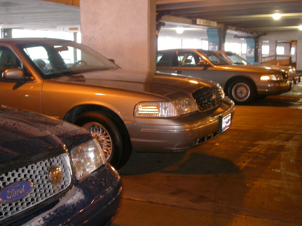 Gold Ford Crown Victoria front three-quarter in parking garage beside dark blue Crown Vic