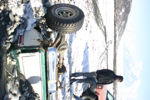 2003 Jeep TJ - An off-road vehicle is stuck in a snowy and muddy environment, with a person standing nearby.