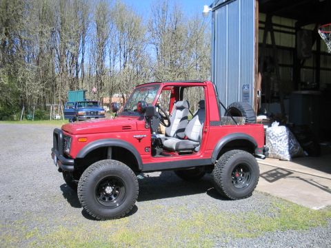 1987 Suzuki Samurai - A red Suzuki Samurai is parked on a gravel lot next to a metal building, with another truck visible in the background.
