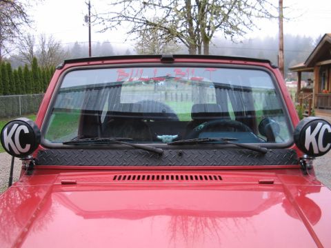 1987 Suzuki Samurai - This red SUV features KC lights and custom text on the windshield, but its year and model are not definitively identifiable from this image.