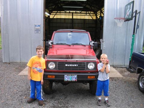 1987 Suzuki Samurai - Two boys pose with a red 1987 Suzuki Samurai in front of a garage.