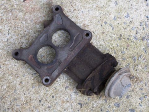 1979 Ford F-150 - A rusty, cast iron automotive part, possibly an exhaust manifold component, rests on a concrete surface.