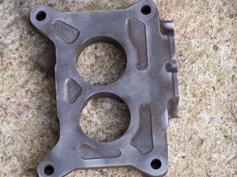 1979 Ford F-150 - A metal carburetor spacer with two large circular openings is shown, likely for an engine component.