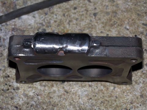 1979 Ford F-150 - Cast iron carburetor spacer with a metal tube modification, shown on a concrete surface.