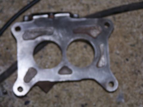 1979 Ford F-150 - A metal gasket with two large circular openings and mounting holes lies on a textured surface.