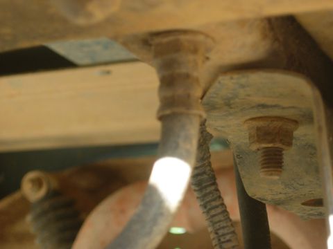 1995 Ford Bronco - This image shows a close-up view of a rusty bolt and bracket on the underside of a vehicle, with some hoses and wiring visible.