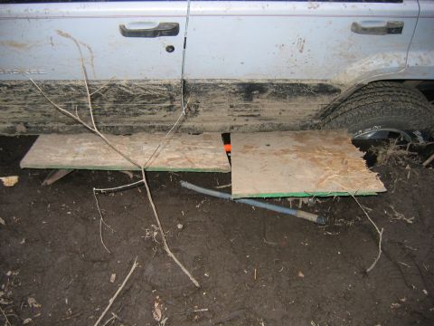 1995 Ford Bronco - A muddy Jeep Cherokee is stuck in the dirt with plywood placed under its doors.