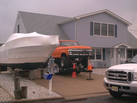 2005 Ford Excursion - A vintage orange Ford pickup truck is parked on a trailer in front of a house, with a boat covered in plastic to its left and a white Ford…