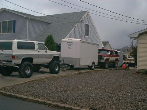 2005 Ford Excursion - Two pickup trucks and a trailer are parked in a driveway next to a house.
