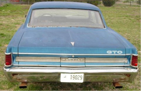 1964 Pontiac Tempest - The rear of a blue 1964 Pontiac GTO sedan is shown, its distinctive taillights and chrome bumper.