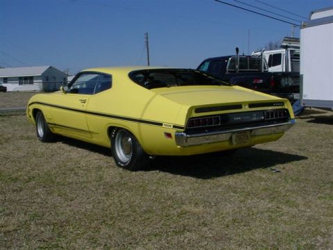 1972 Ford Ranchero - Rear view of a yellow 1970s Ford Ranchero with a black stripe, parked outdoors near other vehicles.