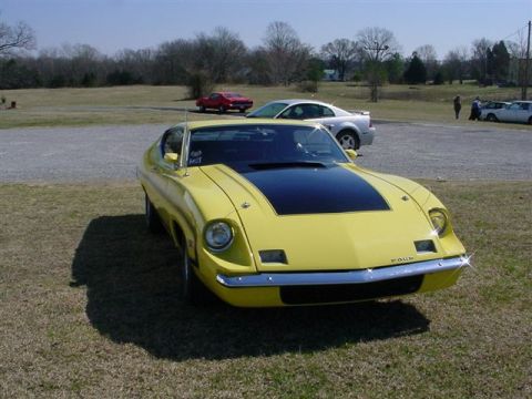 1972 Ford Ranchero - A yellow coupe with a black hood stripe sits in a grassy lot with other vehicles in the background.