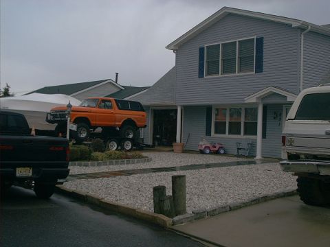 2005 Ford Excursion - An orange Ford Bronco is parked on a trailer in front of a house, with other vehicles present.