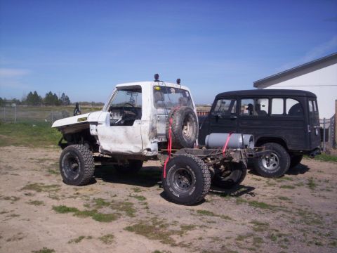 1978 Ford Bronco - Two vehicles are parked outdoors under a clear blue sky. The foreground vehicle is a white truck chassis, and a black SUV is visible behind…