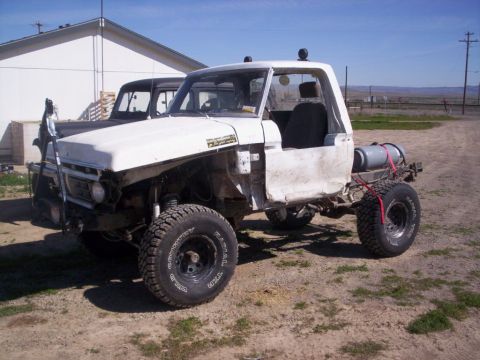 1978 Ford Bronco - A heavily modified pickup truck sits in a dirt lot next to another vehicle under a clear sky.