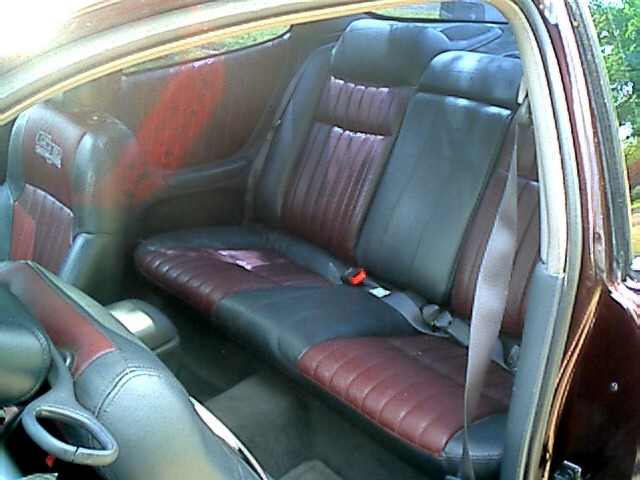Back seat of a car with dark gray and maroon leather seats. A pinkish item is on the seat