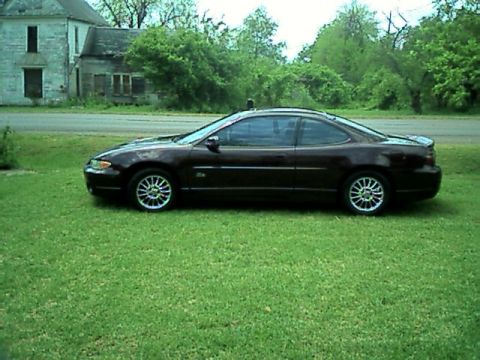 2002 Pontiac Grand Prix - A dark red 2002 Pontiac Grand Prix coupe is parked on a grassy lawn in front of an old house.