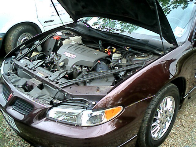 Front of a 2002 Pontiac Grand Prix with hood open showing the engine. Another vehicle is partially visible to the left