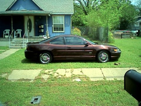 2002 Pontiac Grand Prix - A maroon Pontiac Grand Prix is parked on the grass in front of a residential house.
