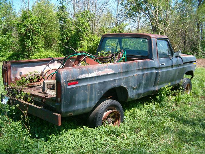 Rusty 1970s pickup truck with flat tires, overgrown with weeds