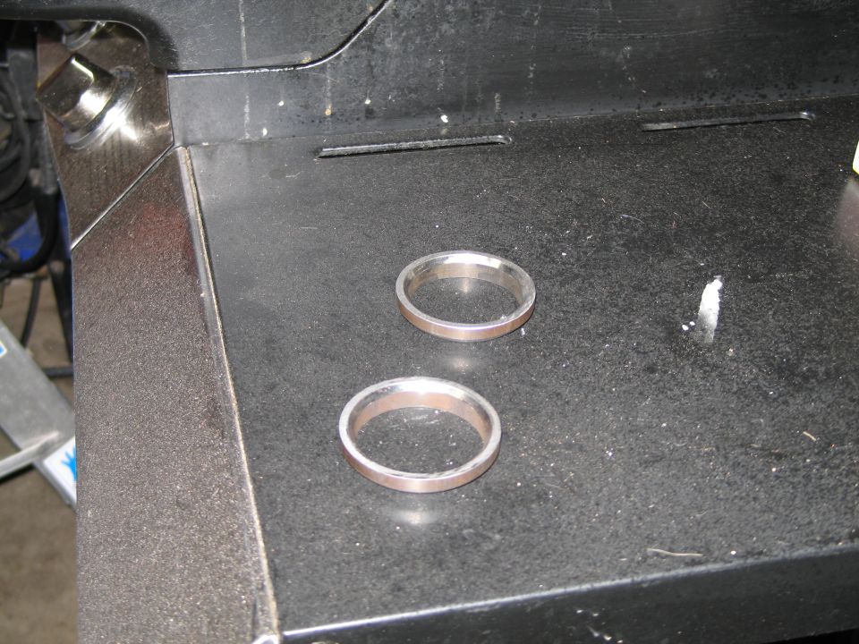 Two machined aluminum rings on a black steel workbench