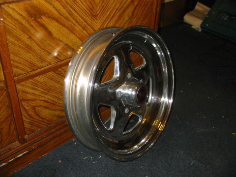 1985 Ford LTD Crown Victoria - A single chrome wheel with a five-spoke design is shown, resting on a dark carpeted surface.