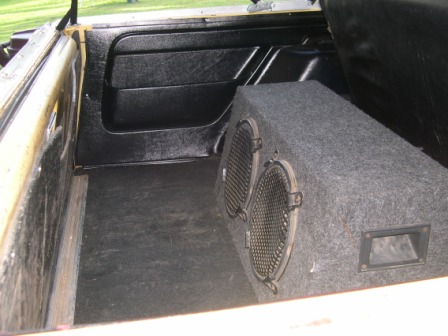 1982 Ford Bronco - The cargo area of a vehicle shows a large subwoofer box and black interior trim.