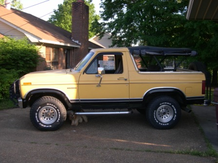 1982 Ford Bronco - A yellow 1982 Ford Bronco is parked in front of a house with a tree in the background.