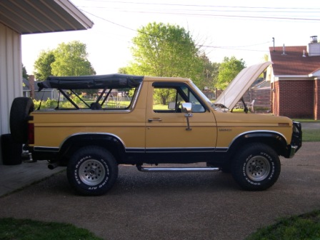 1982 Ford Bronco - A yellow Ford Bronco from the early 1980s is parked outside with its hood up and a soft top in place.