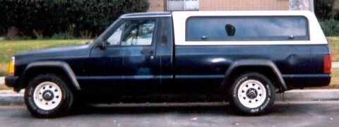 1986 Jeep Comanche - A 1986 Jeep Comanche pickup truck with a white camper shell is parked on a street.