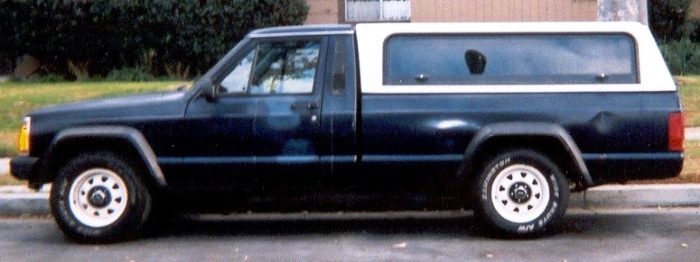 Dark blue Jeep Comanche pickup with white camper shell, side view at curb