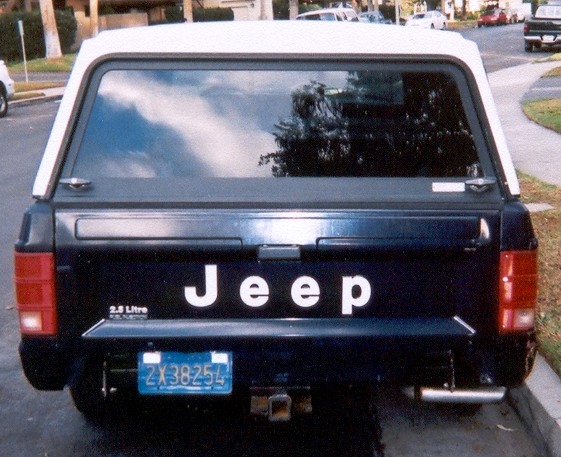 Rear of dark blue Jeep Comanche pickup with white camper shell and JEEP tailgate lettering