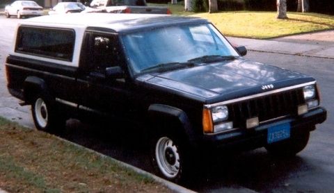 1986 Jeep Comanche - A black 1986 Jeep Comanche pickup truck with a white camper shell is parked on a residential street.
