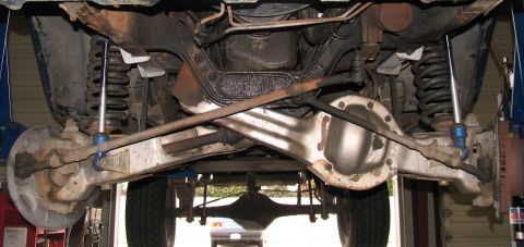 1984 Ford Bronco - The underside of a vehicle is shown, focusing on the front axle and suspension system. The image displays various mechanical components in…