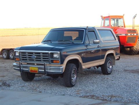 1986 Ford Bronco - This 1986 Ford Bronco is parked next to a large red tractor in an outdoor setting.