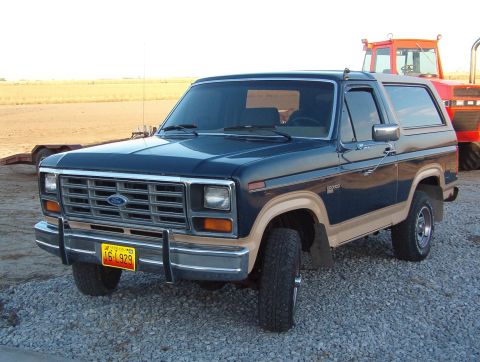 1986 Ford Bronco - This Ford Bronco is parked on gravel with a large red tractor in the background.