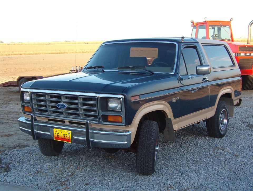Dark blue and tan Ford Bronco parked on gravel, with a red tractor behind it