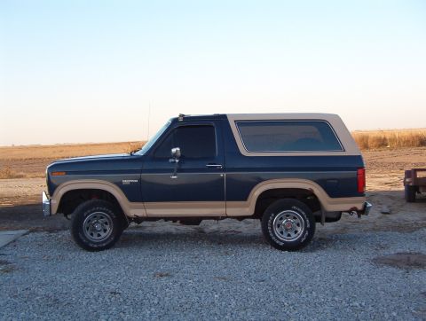 1986 Ford Bronco - A two-tone Ford Bronco is shown from the side, parked outdoors on a gravel surface.