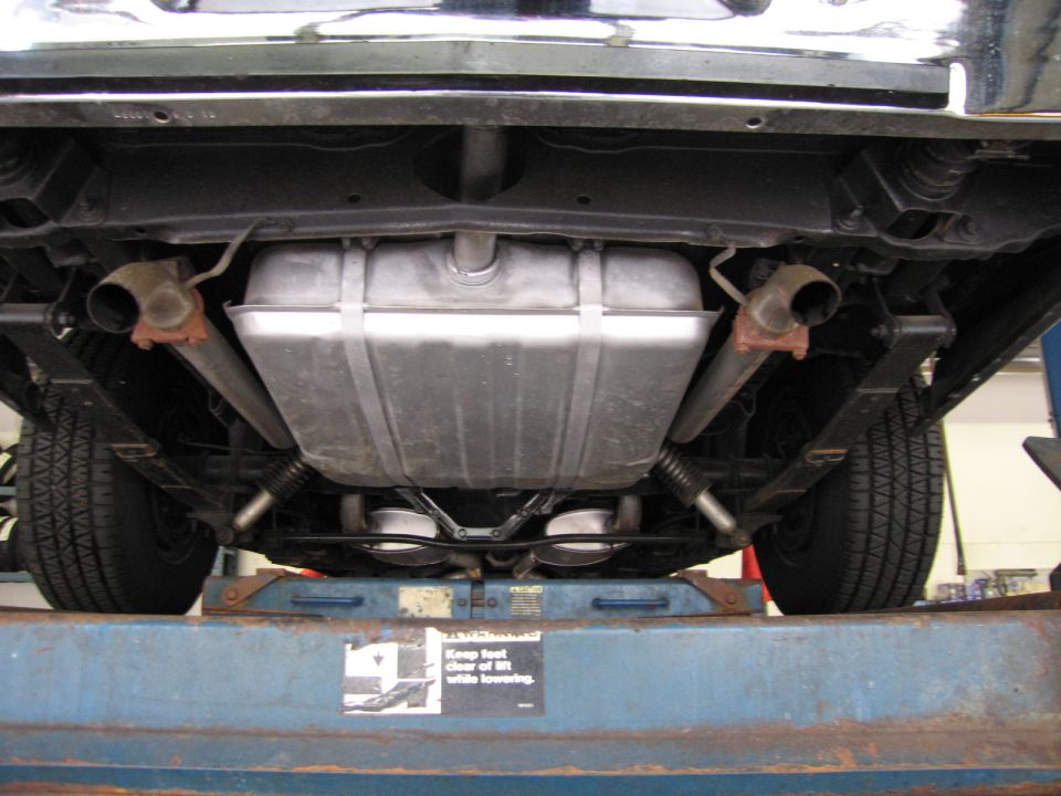 Undercarriage view of a car on a lift showing fuel tank, dual exhaust, and rear suspension