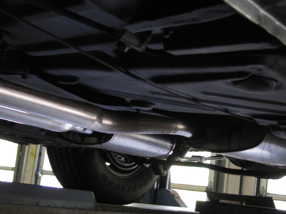 Vehicle undercarriage on lift showing exhaust pipes, muffler, and Goodyear tire