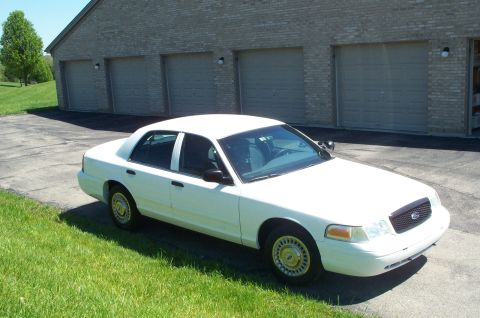 2001 Ford Crown Victoria - This white 2001 Ford Crown Victoria is parked in front of a brick building with three garage doors.