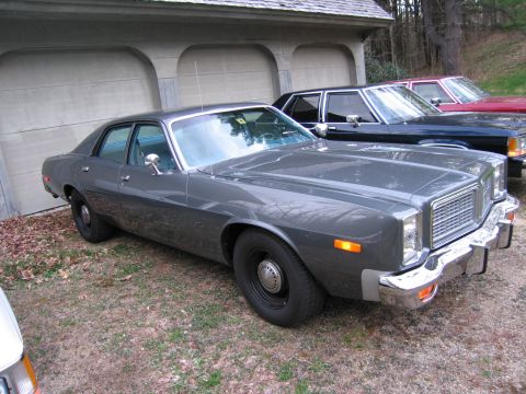 1978 Dodge Monaco - A 1978 Dodge Monaco sedan is parked in front of a garage, with two other vehicles visible behind it.