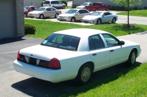 2001 Ford Crown Victoria - A white 2001 Ford Crown Victoria sedan is parked in a driveway with other vehicles in the background.