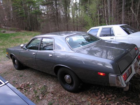 1978 Dodge Monaco - A dark gray sedan is parked outdoors next to a white car, with trees in the background.